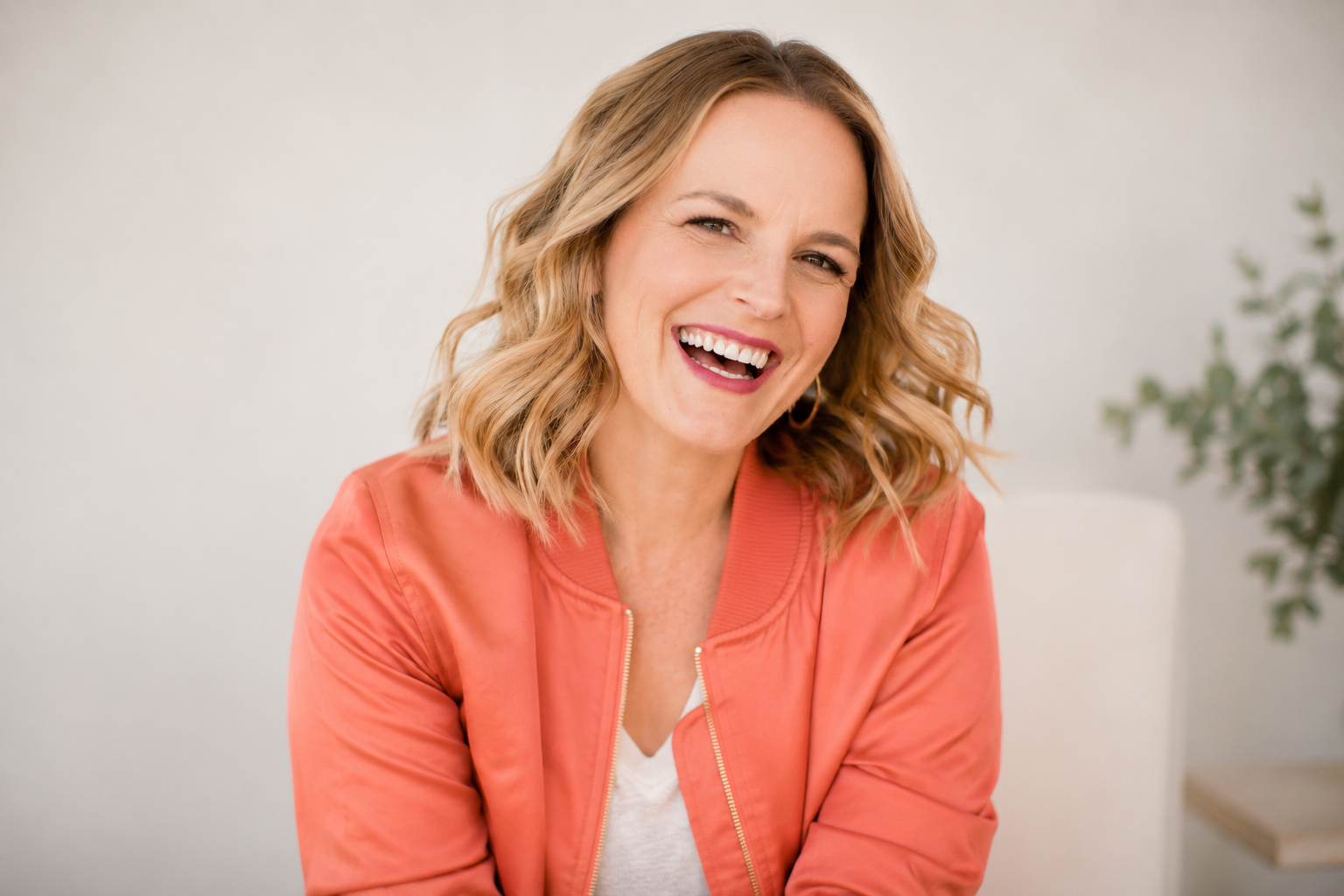 Ash, laughing, in a coral bomber jacket